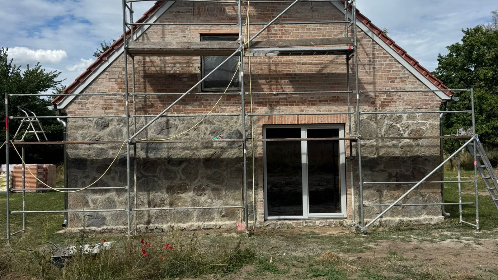 Renowacja szczytu domu z kamienia polnego i starej cegły – rusztowanie, nowe drzwi tarasowe
