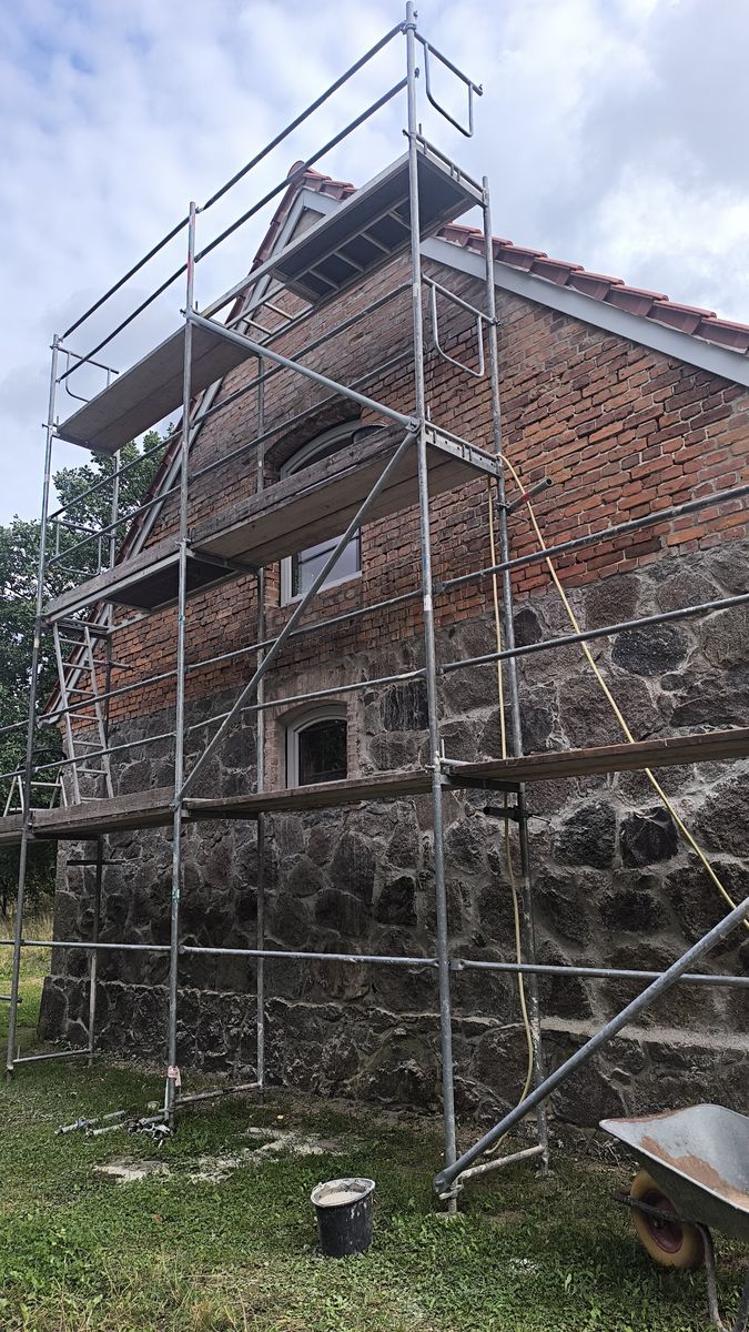 Ściana boczna starego domu z kamienia i cegły na rusztowaniu w trakcie renowacji