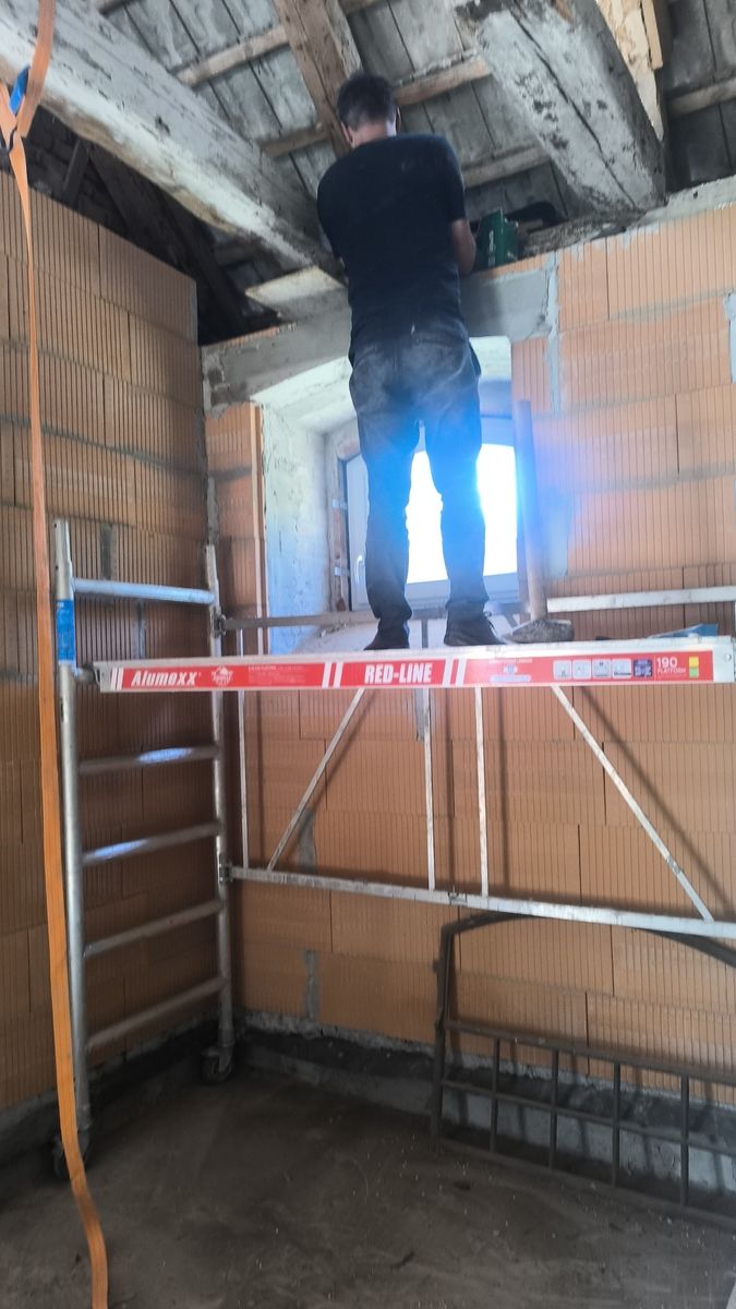 Murowanie ścian z pustaków ceramicznych na poddaszu, pracownik na rusztowaniu